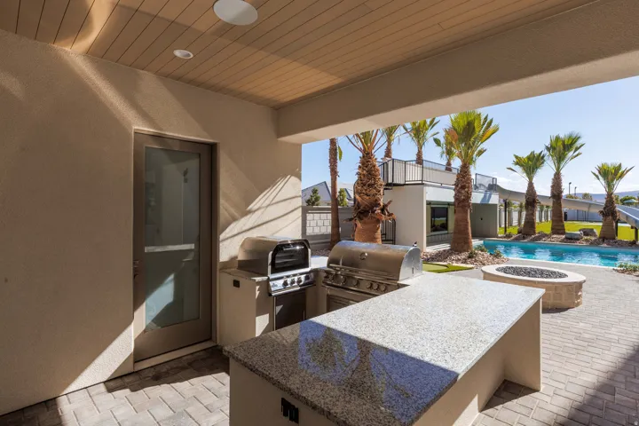 Covered patio featuring a built-in outdoor kitchen with stainless steel grills, a stone countertop, and recessed lighting