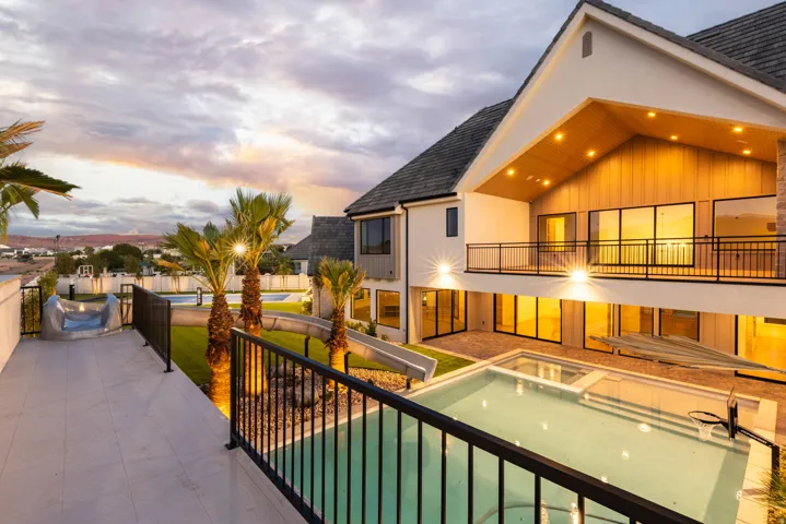 Exterior featuring a multi-level design, a swimming pool with integrated spa, an upper-level balcony with metal railings, a lower-level patio, and multiple sliding glass doors