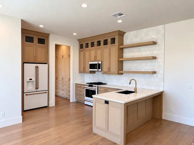Kitchen featuring wood-finish cabinetry, white tile backsplash, a center island with sink, and recessed lighting