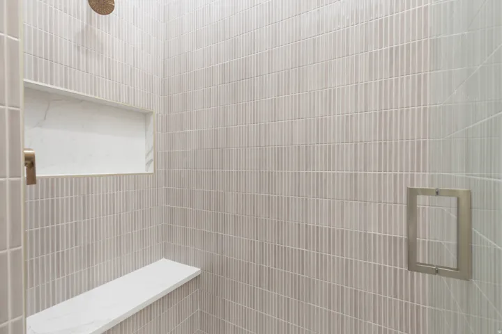 Vertical tile wall finish, built-in shower niche with stone finish, built-in shower bench with stone finish, and a round shower head
