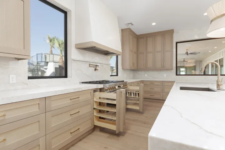 Gourmet kitchen featuring custom cabinetry, light-toned countertops, a built-in range, pull-out spice racks, and a large window