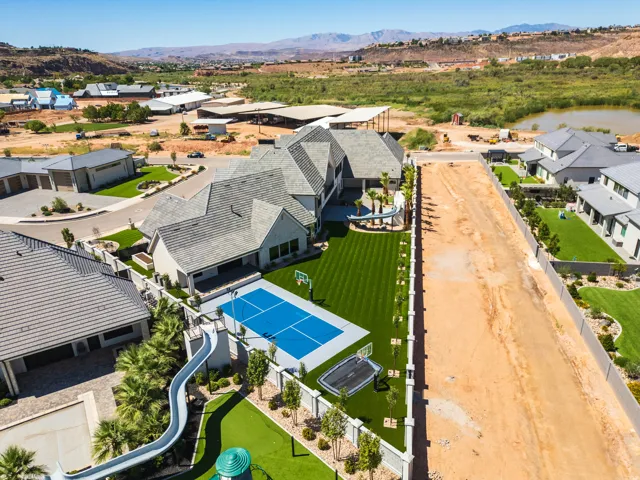 Expansive backyard featuring a blue hard court, a large slide, a built-in trampoline, and artificial turf lawn