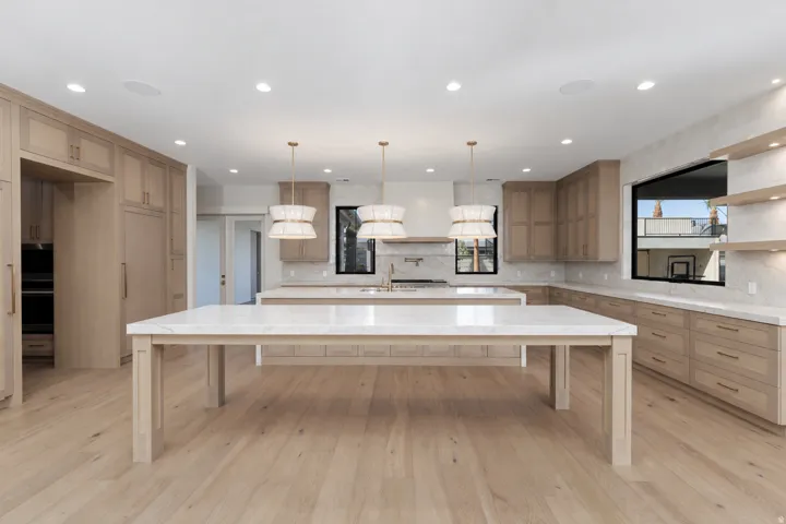 Gourmet kitchen featuring a large waterfall-edge island with wood-finish base, white quartz countertops, custom wood cabinetry with integrated appliances, pendant lighting, and recessed ceiling lights