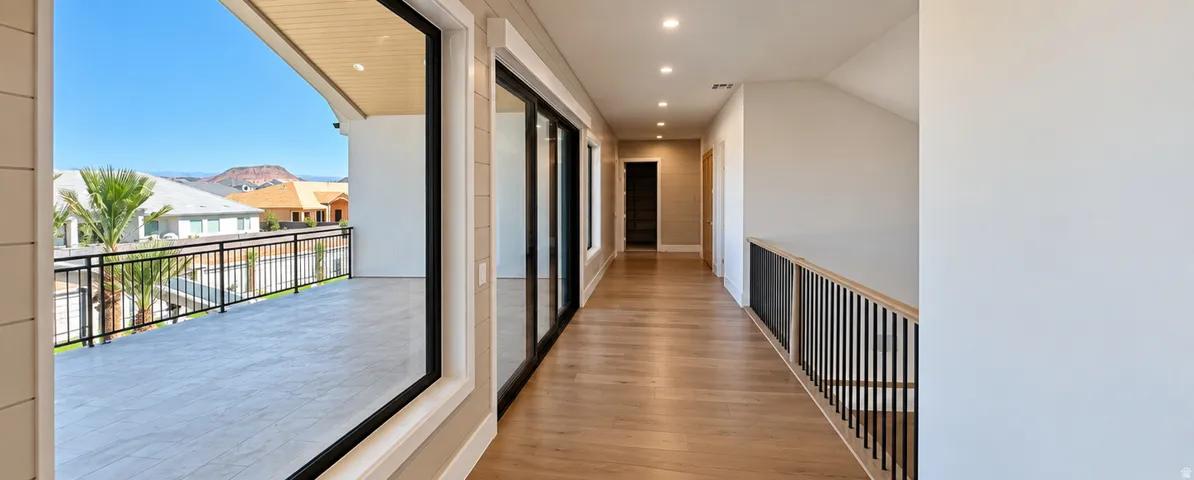 Upper-level hallway with wood-finish flooring, recessed lighting, and a metal baluster railing system