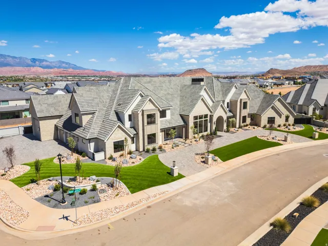 Expansive residence featuring a multi-gabled roofline, stone and stucco exterior, multiple large windows, and a meticulously landscaped yard with a curved driveway