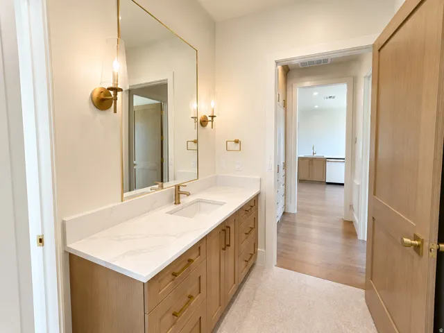 Vanity with light wood-finish cabinetry, white countertop with integral sink, and brass fixtures