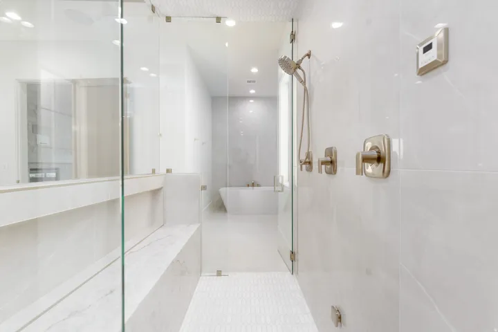 Walk-in shower with clear glass enclosure, large format white wall tiles, and a built-in bench