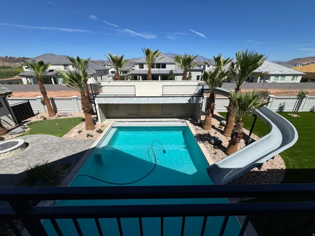 Outdoor swimming pool with an integrated slide, surrounded by artificial turf and mature palm trees