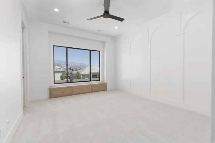 Wall paneling with arch detailing, built-in window seating with storage, recessed lighting, ceiling fan, and carpet flooring