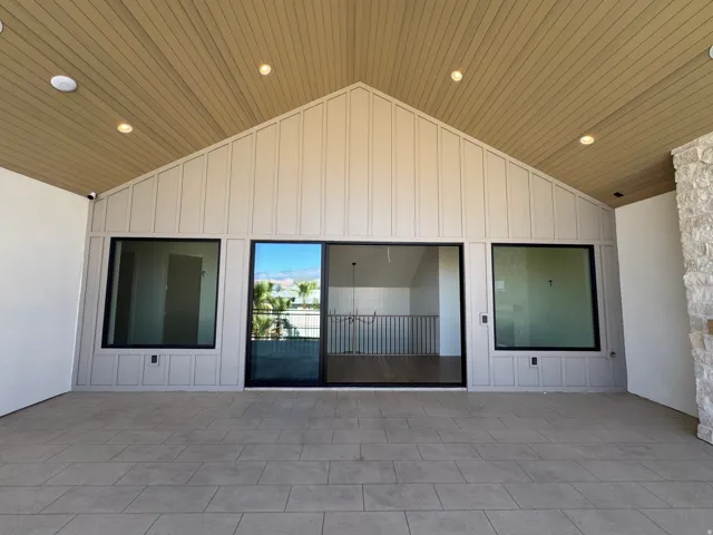 Expansive outdoor patio with large format tile flooring, a vaulted wood-finish ceiling, recessed lighting, board and batten siding, and large sliding glass doors