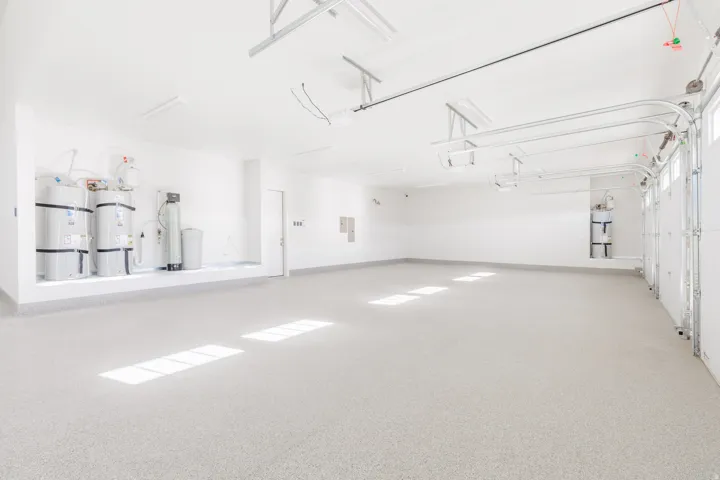 Spacious garage with light-colored epoxy flooring, bright overhead lighting, and multiple water heaters
