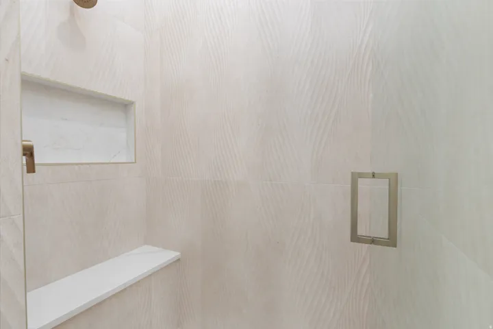 Textured tile shower surround with a built-in niche, integrated shower bench, and a brushed nickel shower handle