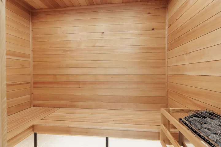 Wood-paneled sauna featuring built-in bench seating and an integrated heater with stones