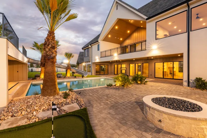 Expansive paver patio with a built-in fire pit, swimming pool, and dedicated putting green
