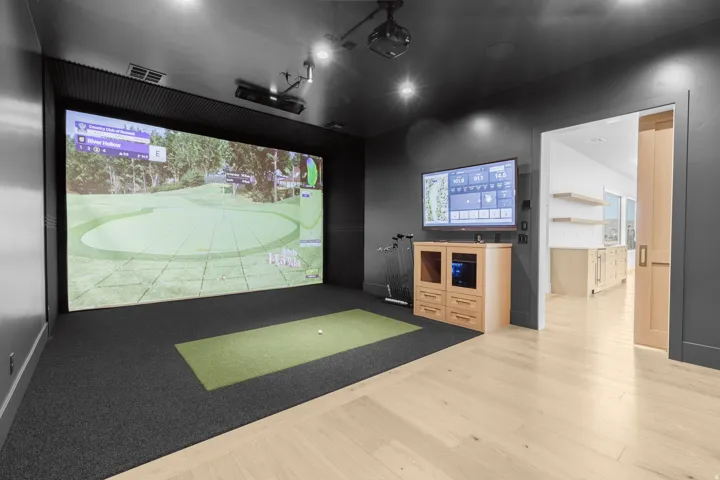 Dedicated golf simulator room featuring a large projection screen and putting surface