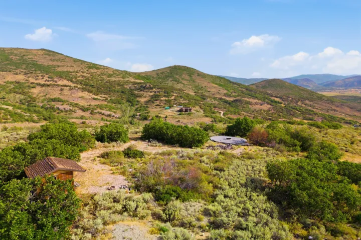 Expansive mountainous landscape with natural vegetation, featuring a distant structure and a circular pad