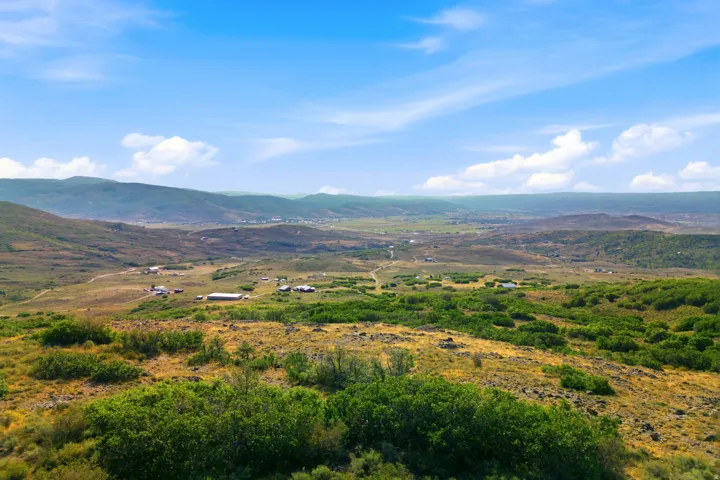 Expansive rural landscape with rolling hills, distant mountain ranges, and scattered structures