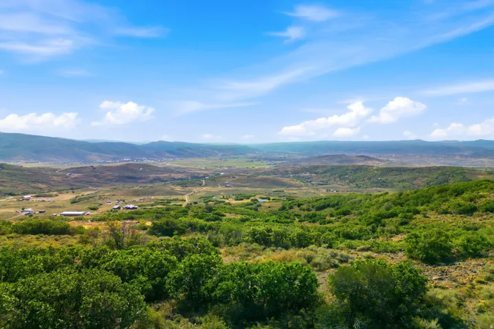 Expansive landscape featuring rolling hills, varied green foliage, distant mountains, and a clear sky with scattered clouds