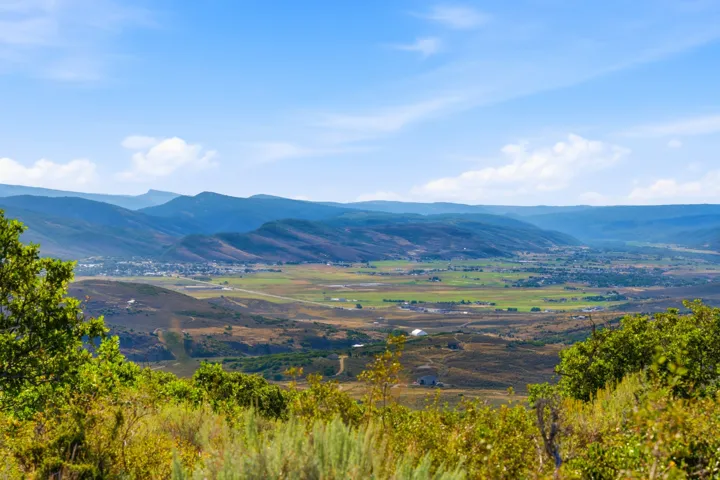 Expansive valley scenery featuring distant mountainous terrain, a clear blue sky, and a mix of green and arid natural landscaping