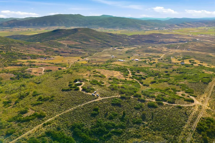 Expansive mountainous and valley terrain with scattered green foliage and visible dirt roads