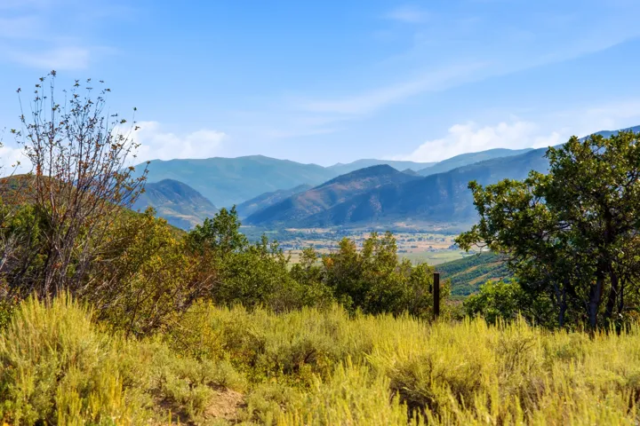Expansive natural landscape with distant mountain ranges, a valley, and varied vegetation