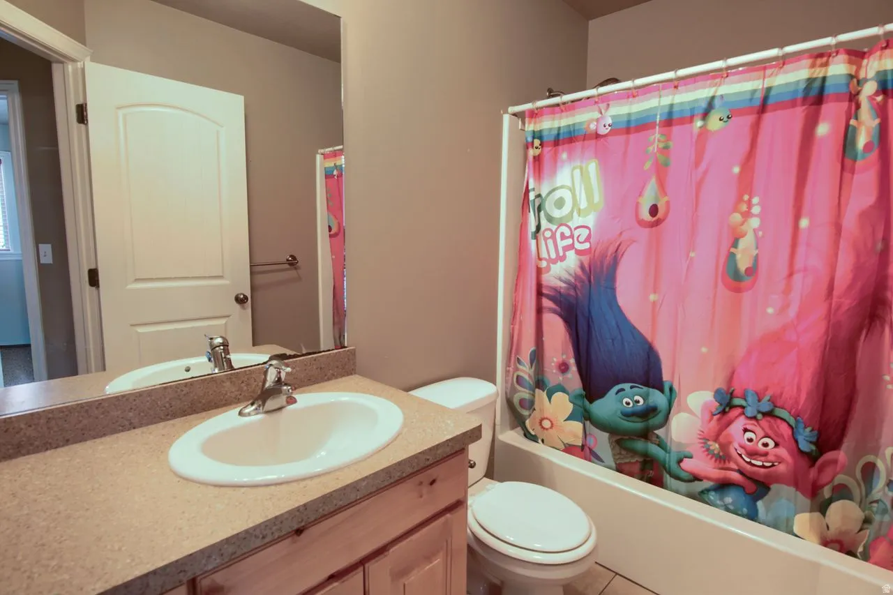Bathroom featuring a vanity with a light-toned countertop and an integrated sink, a built-in bathtub with a shower, and a toilet