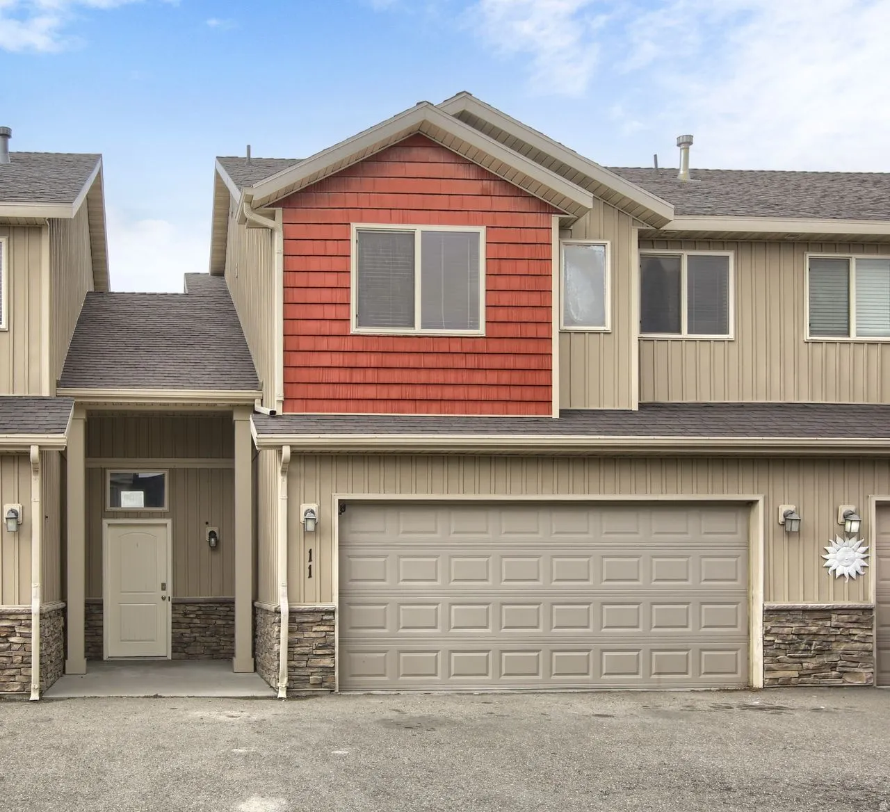 Two-story residence featuring a large garage, partial stone facade, and red shingle siding accents