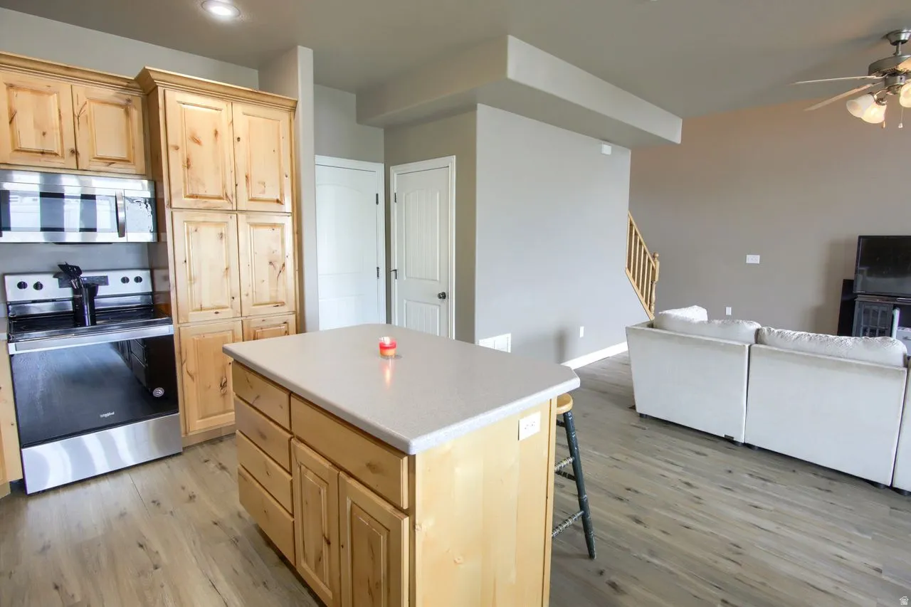 Kitchen island with a light-toned countertop, wood-finish flooring, full-height wood cabinetry, stainless steel range, and an overhead microwave