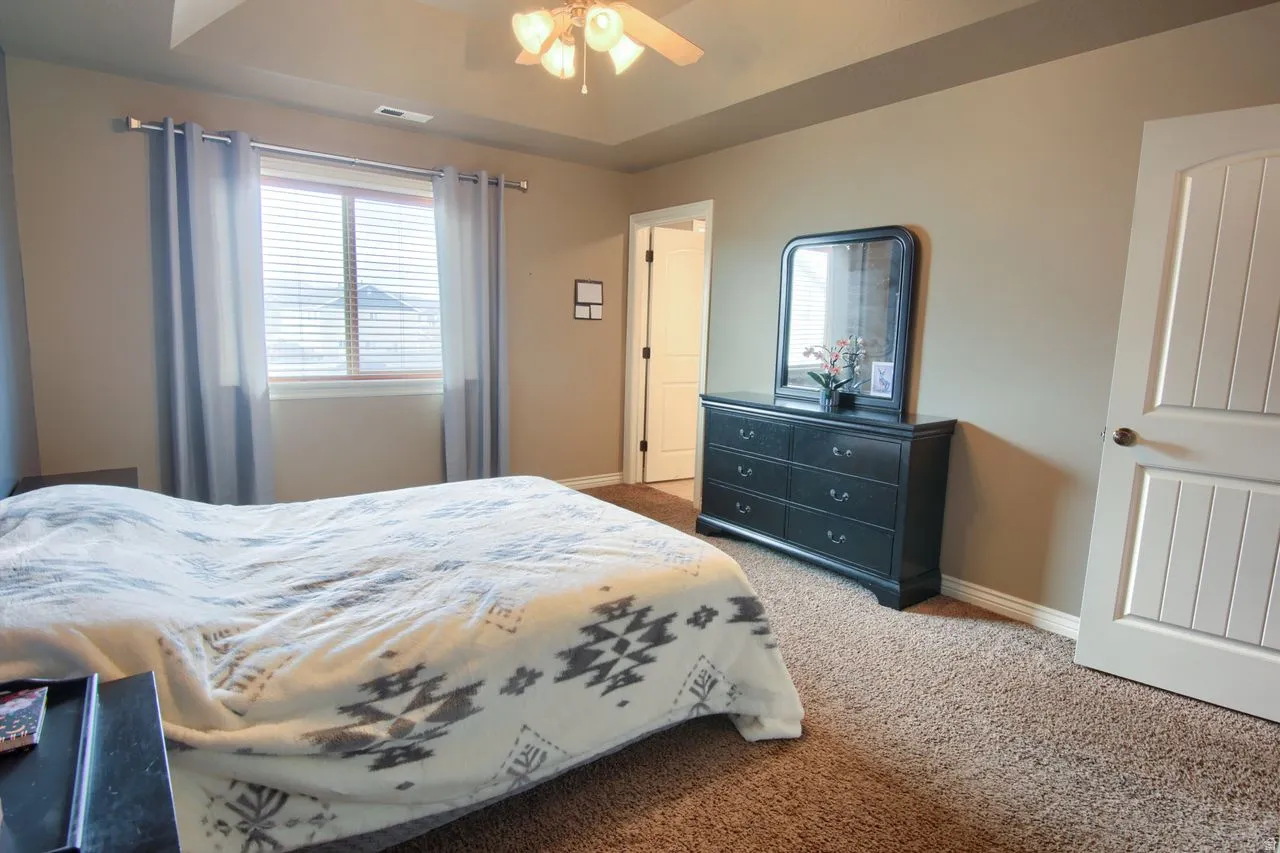 Tray ceiling with a ceiling fan, window with blinds, and white panel doors
