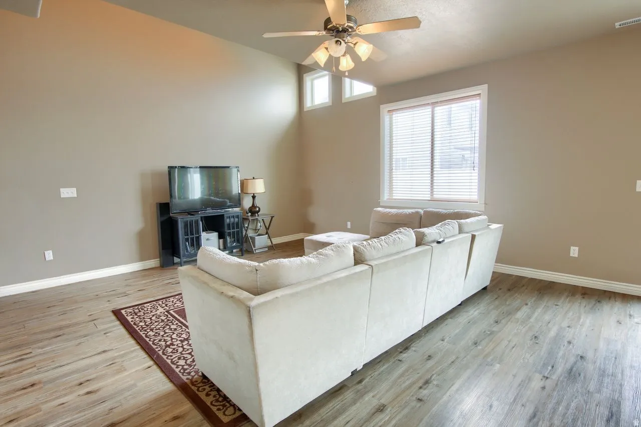 Vaulted ceiling, wood-finish flooring, ceiling fan, large window, and upper accent windows