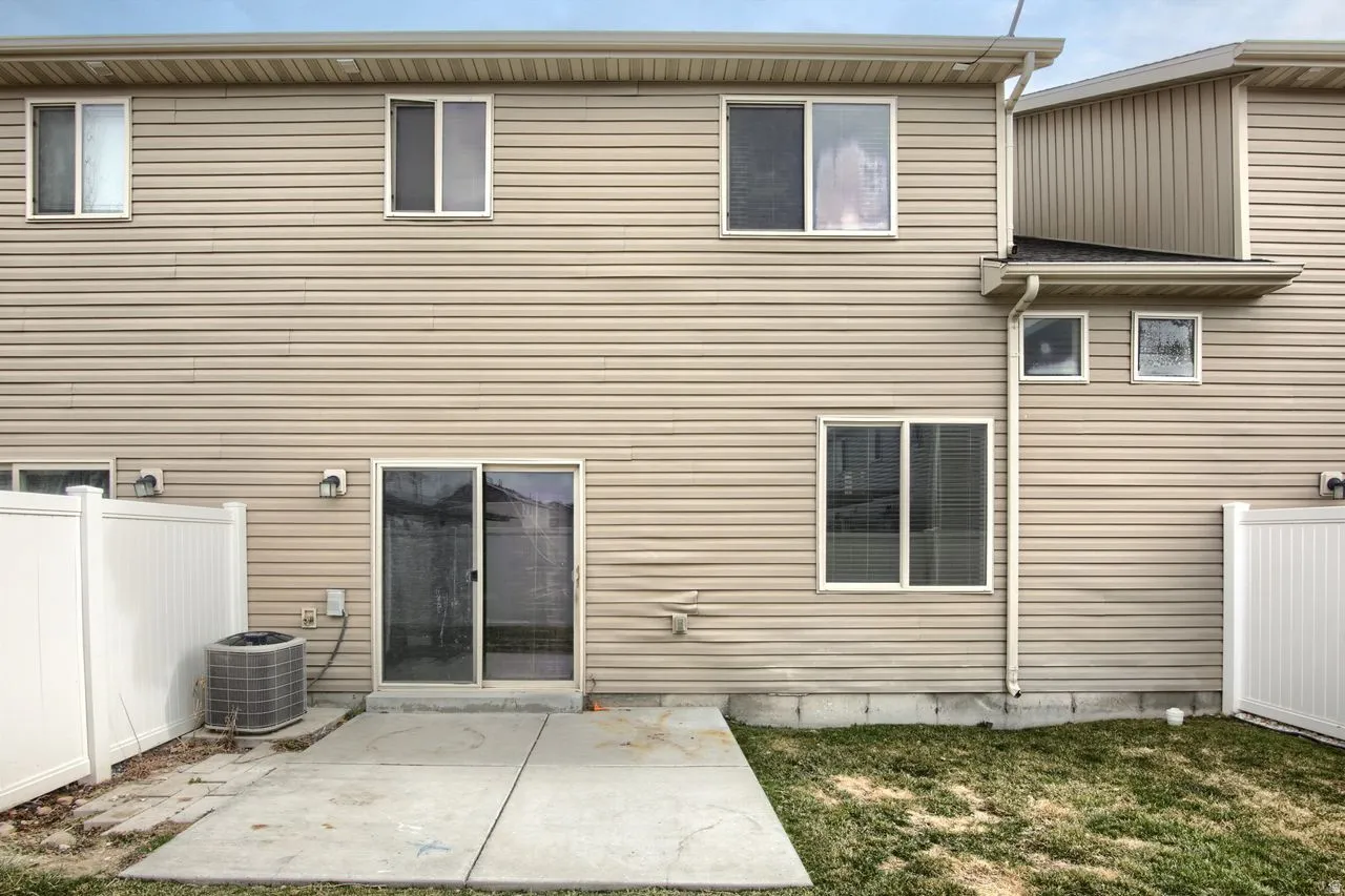 Exterior featuring beige horizontal siding, multiple windows, a sliding glass door, a concrete patio, and a white privacy fence