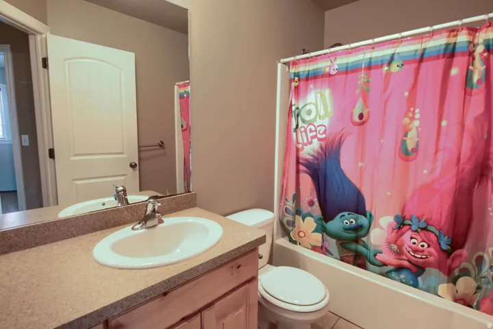 Bathroom featuring a vanity with a light-toned countertop and an integrated sink, a built-in bathtub with a shower, and a toilet