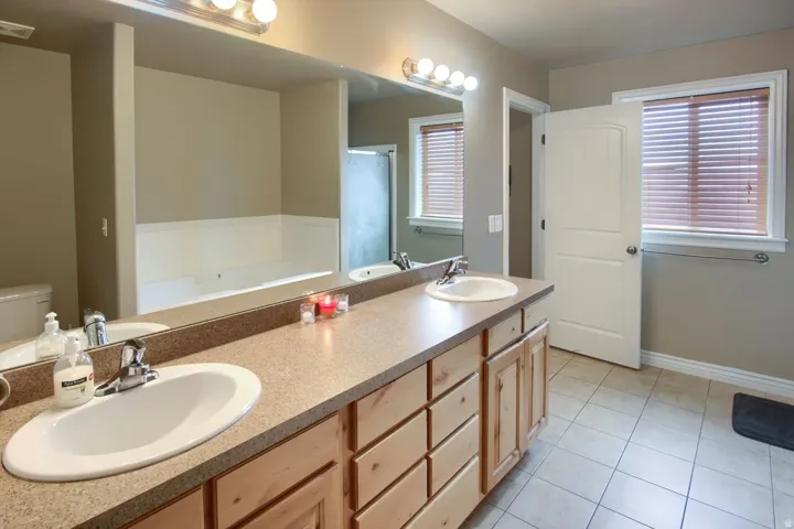 Double vanity with integrated sinks, wood-finish cabinetry, a large mirror, and overhead strip lighting