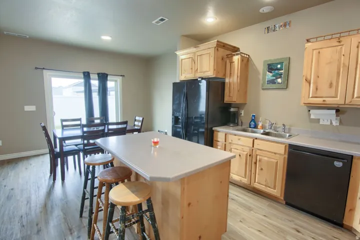 Kitchen featuring wood-finish flooring, light wood cabinetry, a double basin sink, and black appliances