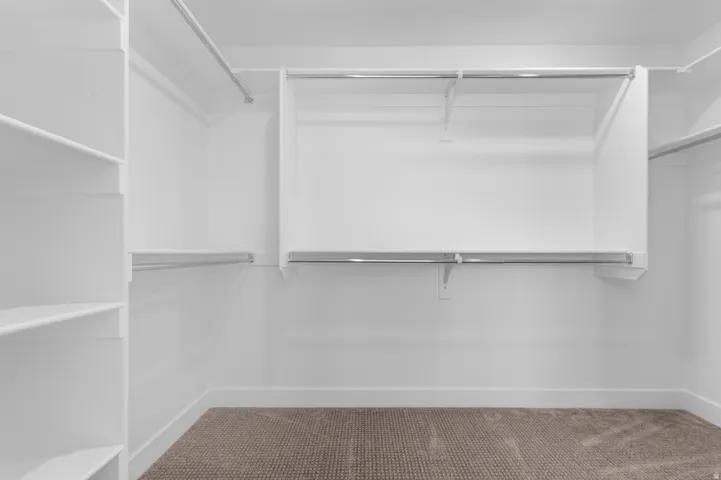 Built-in shelving, multiple hanging rods, and neutral carpeting