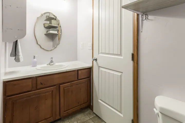 Vanity with a white countertop and wood-finish cabinetry, featuring an oval mirror with a decorative frame