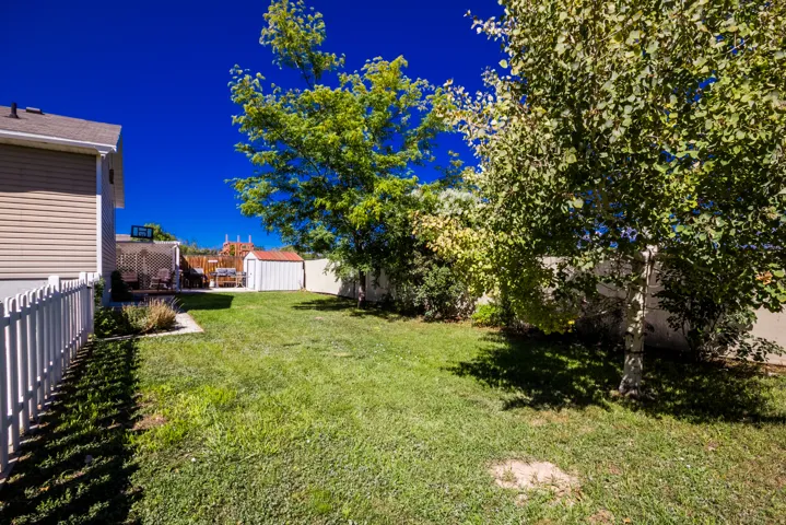 Expansive backyard featuring a manicured lawn, established trees, white picket fencing, and a storage shed