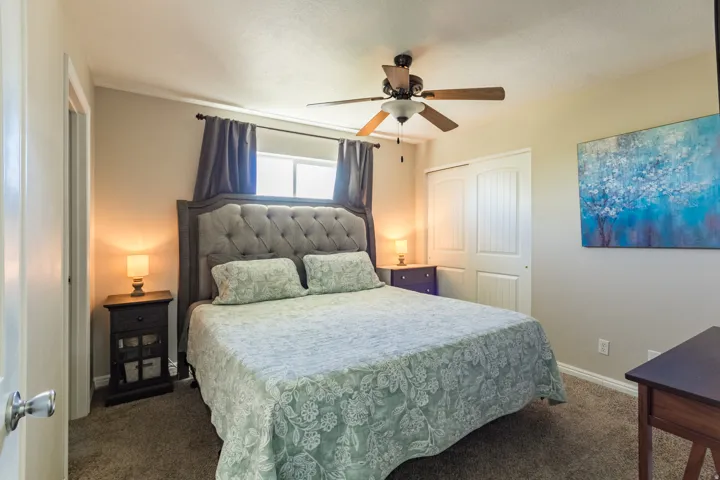 Neutral tone wall paint, carpeted flooring, window with privacy blinds, dual sliding closet doors, and a ceiling fan with light fixture