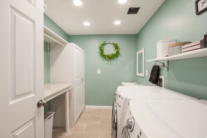 Recessed lighting illuminates this functional laundry space, featuring white built-in cabinetry, a utility sink, and a built-in countertop