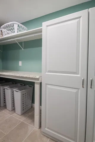Recessed panel cabinetry with brushed nickel hardware, tiled flooring, built-in shelving, and a counter workspace