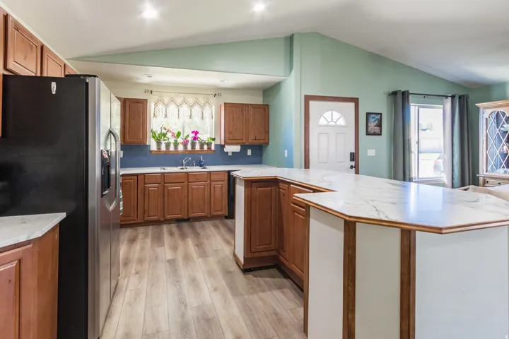 Kitchen featuring wood-finish flooring, white marble-finish countertops, wood cabinetry, a stainless steel refrigerator, and a blue tile backsplash