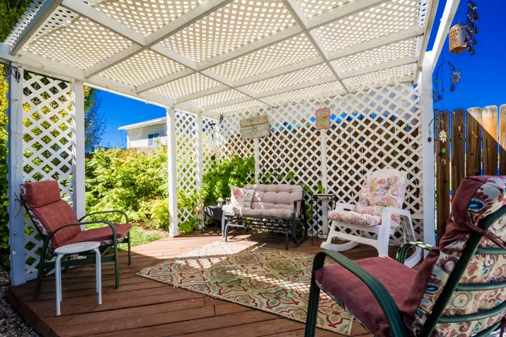 Outdoor patio featuring a white lattice pergola, wood deck flooring, and a privacy fence