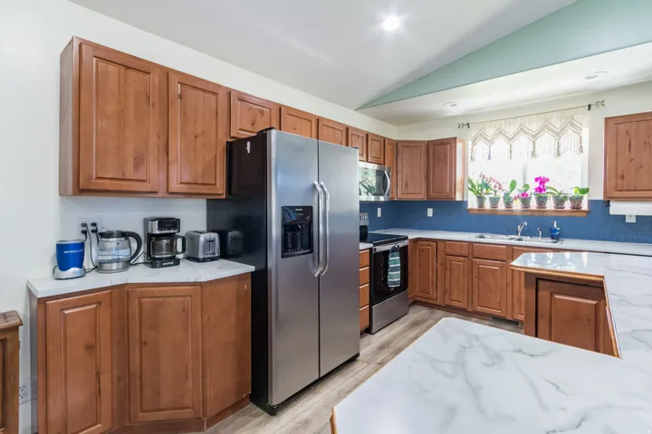 Kitchen featuring wood cabinetry, stainless steel appliances, white marble-look countertops, and a blue tiled backsplash