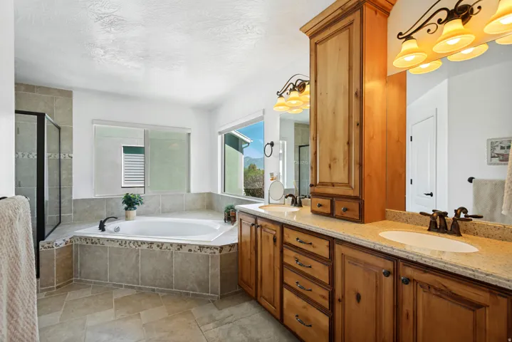 Dual vanity with stone-finish countertops, wood cabinetry, built-in storage, a jetted tub, and a glass-enclosed shower