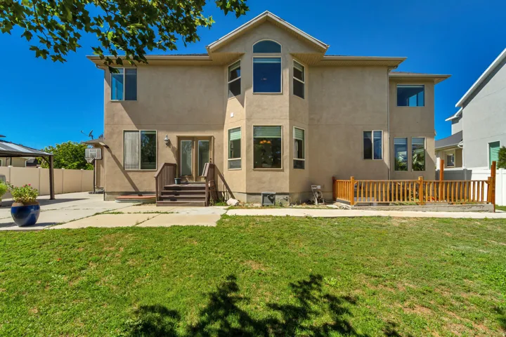 Stucco exterior with multiple windows, second-story bay window, ground-level deck with wood railing, and a grass lawn