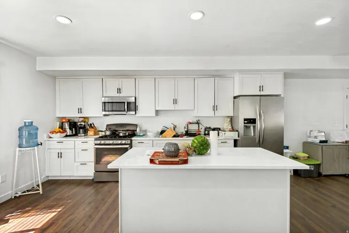 White cabinetry, stainless steel appliances, wood-finish flooring, recessed lighting, and a kitchen island with a light-colored countertop