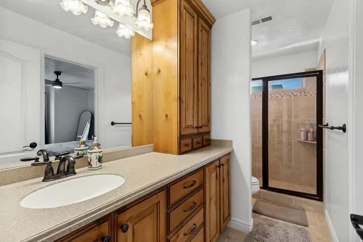 Wood-finish cabinetry with a built-in linen tower, a vanity with an oval sink, a shower enclosure with a dark-framed glass door, and a tiled shower interior with an accent band and built-in shelf