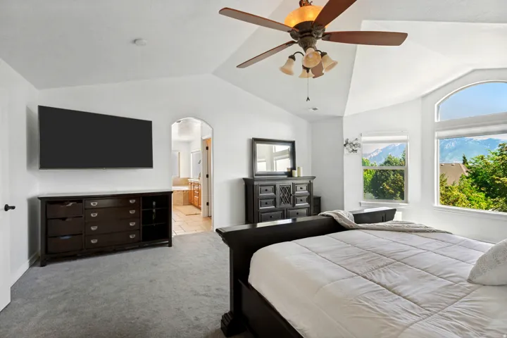 Vaulted ceiling with a ceiling fan, arched doorway, and large arched window