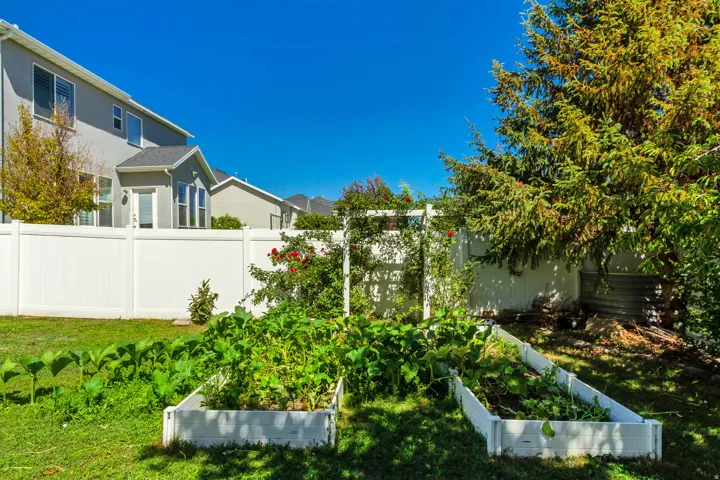Expansive backyard featuring a manicured lawn, two raised garden beds, a white privacy fence, and mature foliage