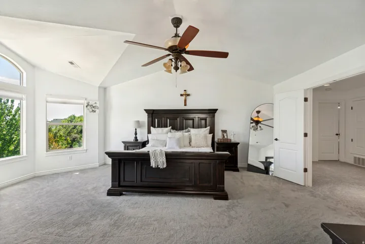 Vaulted ceilings with a ceiling fan light fixture, gray carpet flooring, and multiple windows